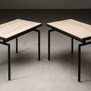 Puede incluir: Dos mesas auxiliares a juego con tapa de travertino beige claro y patas de metal negro. Las mesas tienen un diseño sencillo y moderno de mediados de siglo.