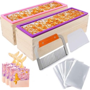 May include: Two wooden soap molds with pink and purple lids, a stainless steel soap cutter, a plastic spatula, and a stack of clear plastic bags. The molds are filled with dried orange petals. Three bars of soap with a mermaid design are in the lower left corner.