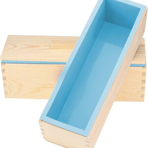 Pode incluir: Um molde de sab&atilde;o de madeira com um forro de silicone azul claro. O molde &eacute; retangular e possui juntas de encaixe. O forro de silicone &eacute; de cor azul claro e se encaixa perfeitamente na estrutura de madeira. Outra caixa de madeira est&aacute; ao fundo.