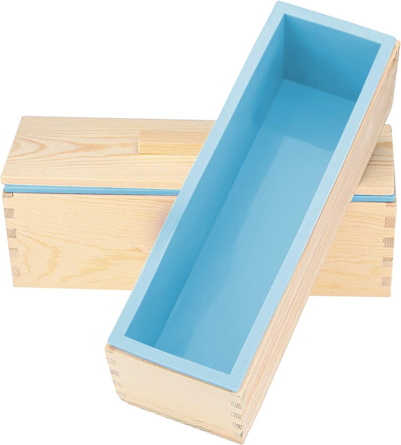 Pode incluir: Um molde de sab&atilde;o de madeira com um forro de silicone azul claro. O molde &eacute; retangular e possui juntas de encaixe. O forro de silicone &eacute; de cor azul claro e se encaixa perfeitamente na estrutura de madeira. Outra caixa de madeira est&aacute; ao fundo.