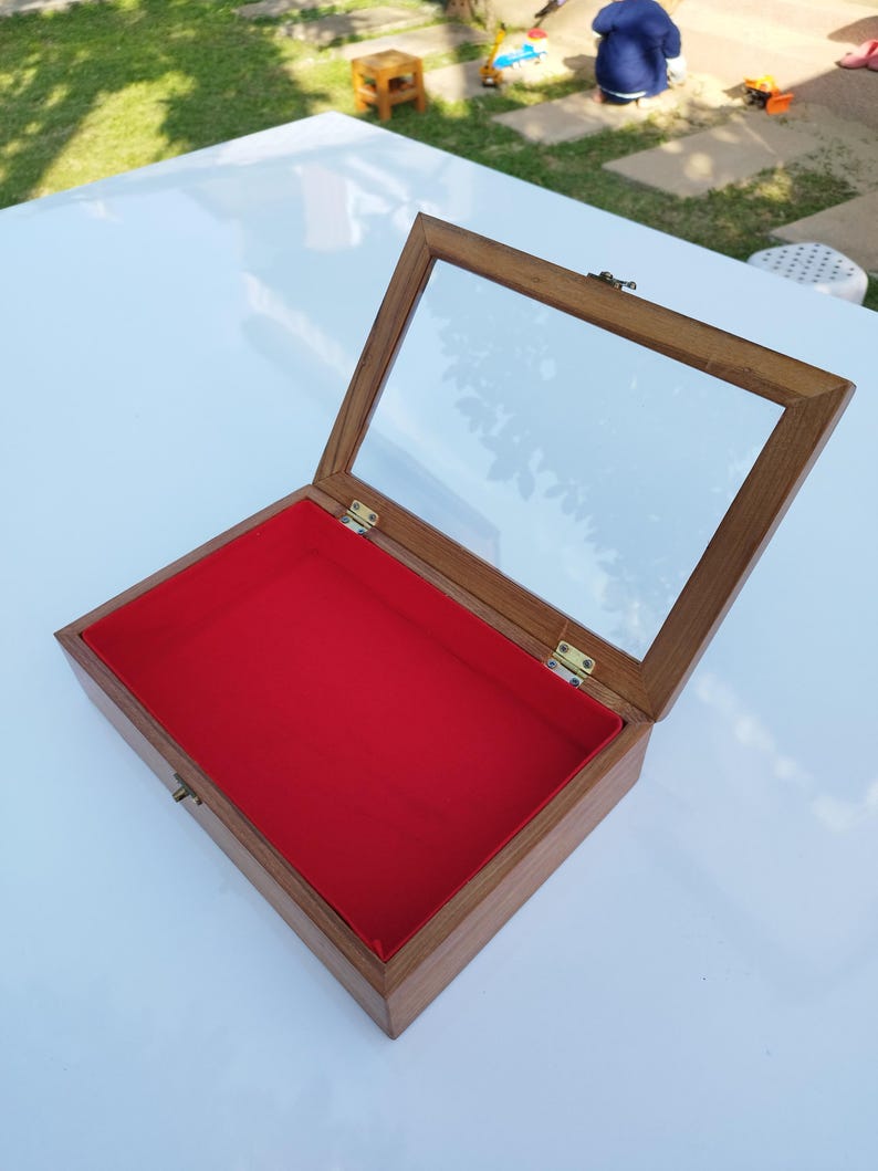 May include: A wooden display box with a glass top and a red velvet lining. The box is open and the lid is propped up.