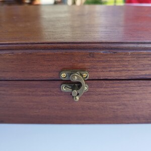 May include: A wooden box with a brass latch. The box has a dark brown stain and a smooth finish.
