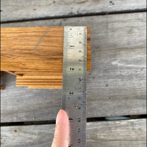 Op de afbeelding: Close-up van een houten plank die met een liniaal wordt gemeten. De liniaal toont een meting van 10 cm.
