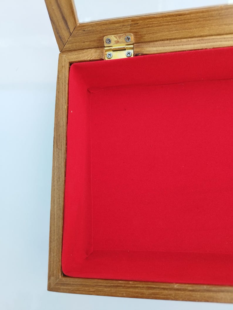 May include: A wooden display case with a glass top and a red velvet interior. The case has a brass hinge.