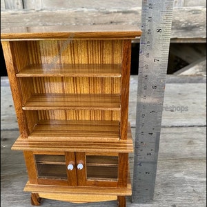 Op de afbeelding: Een miniatuur houten kast met glazen deuren en planken. De kast is ongeveer 18 cm hoog en heeft een bruine houten afwerking.