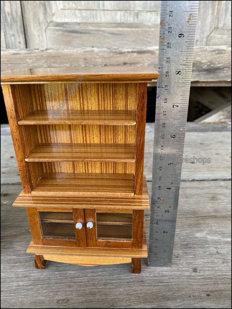 Op de afbeelding: Een miniatuur houten kast met glazen deuren en planken. De kast is ongeveer 18 cm hoog en heeft een bruine houten afwerking.