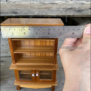 Op de afbeelding: Een miniatuur houten kastje met twee glazen deuren en twee planken. Het kastje is 15 cm hoog en gemaakt van lichtbruin hout.