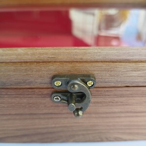 May include: Close-up of a wooden box with a brass latch. The box has a dark wood finish and the latch is closed.