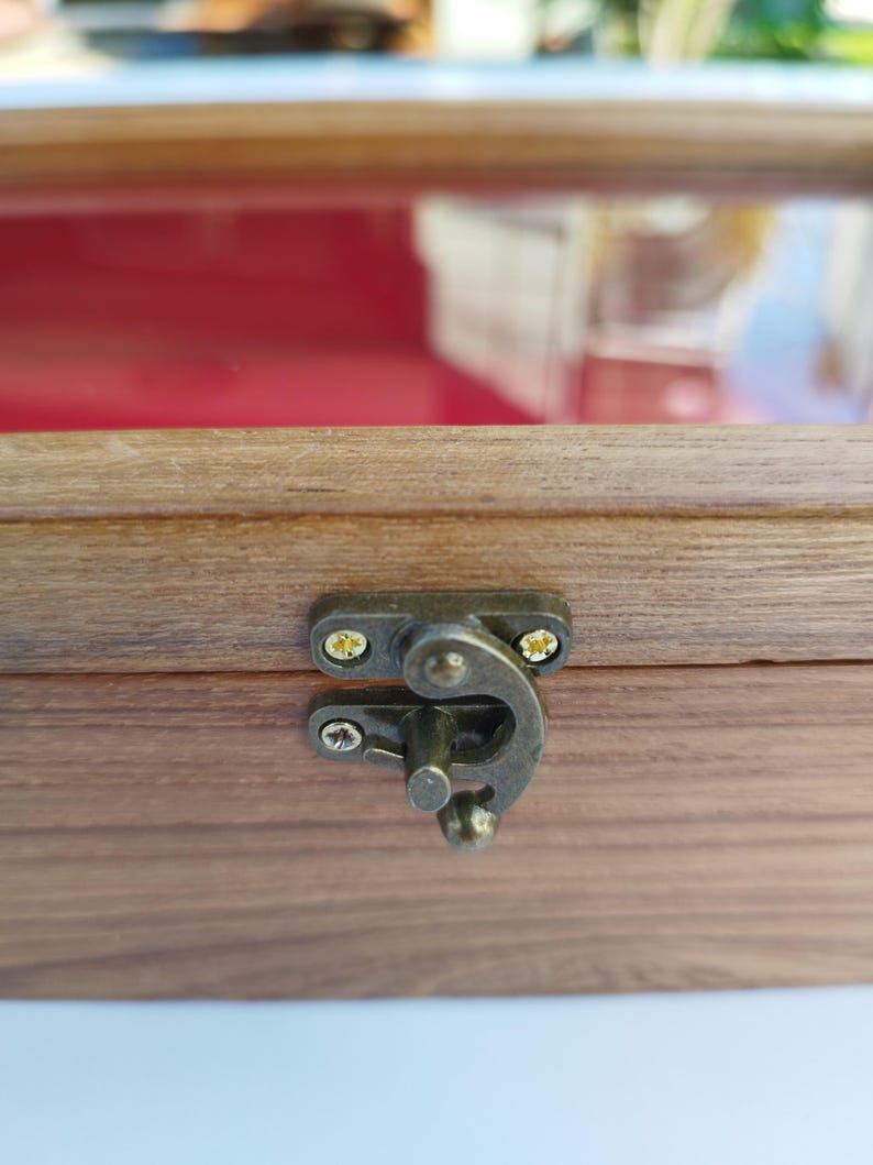 May include: Close-up of a wooden box with a brass latch. The box has a dark wood finish and the latch is closed.