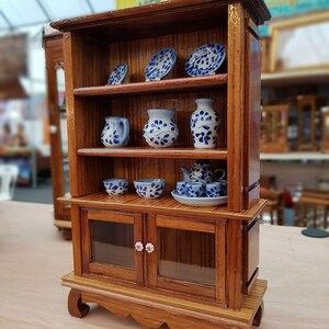 Op de afbeelding: Een houten hutch met twee planken en een kast met glazen deuren. De hutch is versierd met blauwe en witte keramische borden, vazen en kommen. De kast heeft twee roze knoppen.