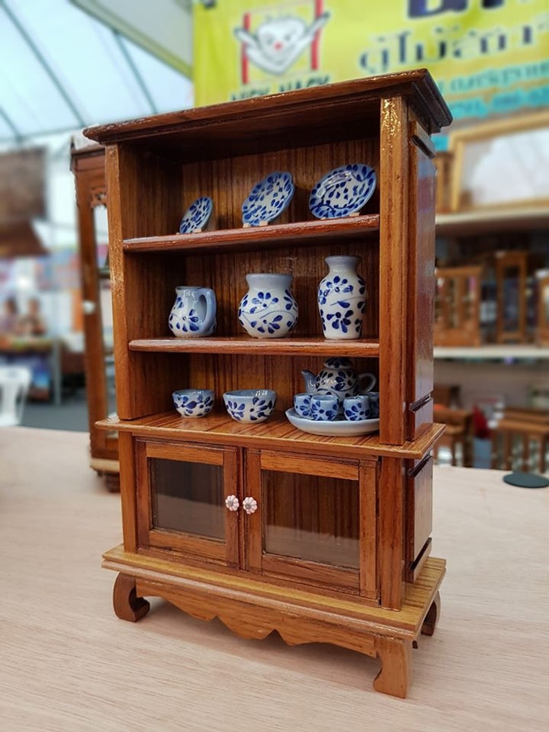 Op de afbeelding: Een houten hutch met twee planken en een kast met glazen deuren. De hutch is versierd met blauwe en witte keramische borden, vazen en kommen. De kast heeft twee roze knoppen.