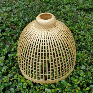 Puede incluir: Una pantalla de lámpara redonda de bambú natural tejido. La pantalla está hecha de tiras de bambú marrón claro tejidas juntas en un patrón de rejilla.