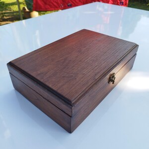 May include: A dark brown wooden box with a hinged lid and a brass latch. The box is made of a rich, dark wood with a smooth finish.