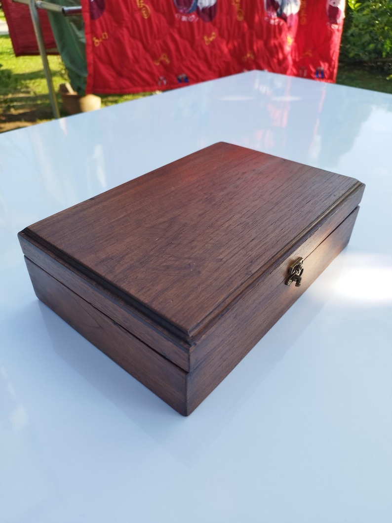 May include: A dark brown wooden box with a hinged lid and a brass latch. The box is made of a rich, dark wood with a smooth finish.