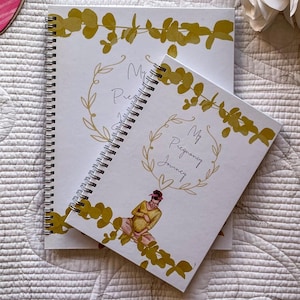 May include: Two spiral bound journals with gold floral designs and the text "My Pregnancy Journey". The smaller journal has a watercolor illustration of a pregnant woman.