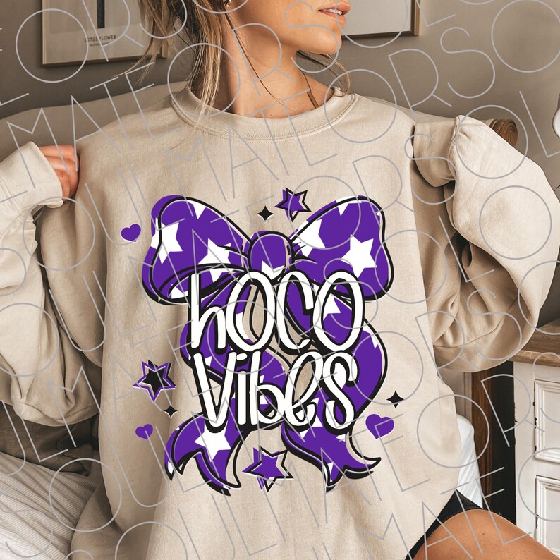 May include: Beige sweatshirt with a purple bow graphic featuring white stars and the words "HOCO Vibes" in white. The design includes purple stars and hearts. A casual, comfortable top.