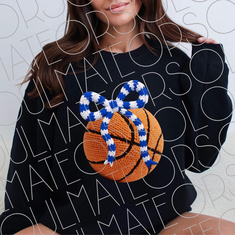 May include: Black sweatshirt featuring a basketball design with a blue and white bow. The basketball is orange with black lines, and the bow is a contrasting blue and white pattern. The sweatshirt is a casual style.