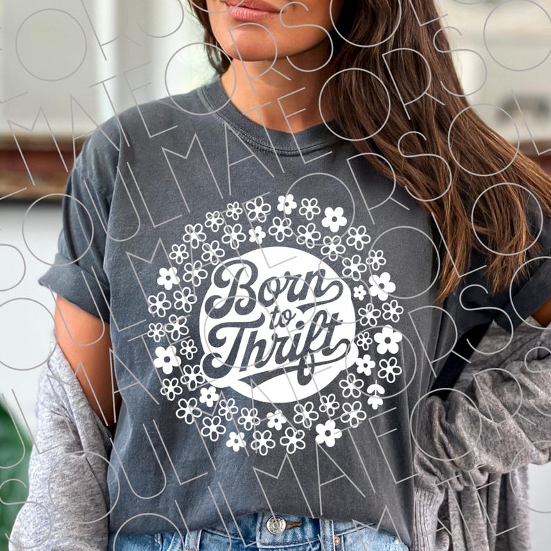 以下が含まれることがあります： 白い花で囲まれた、白い円のデザインに「Born to Thrift」という文字が入った濃い灰色のTシャツ。 シャツは袖をまくり、カジュアルで快適なスタイルです。