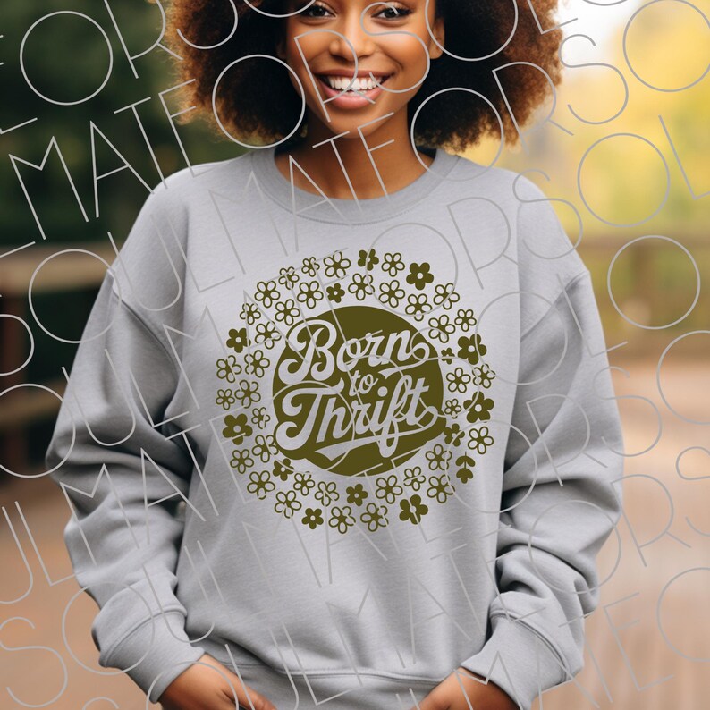 以下が含まれることがあります： 「Born to Thrift」の文字を囲むように花柄がデザインされた、ライトグレーのスウェットシャツ。 文字と花柄はくすんだオリーブグリーンです。 スウェットシャツはクルーネックです。