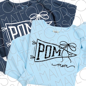 May include: Two long-sleeved sweatshirts, one navy blue and one light blue. The light blue sweatshirt has a black graphic that says "POM mom" inside a pennant shape with bow and arrow details. The navy blue sweatshirt has a similar design.
