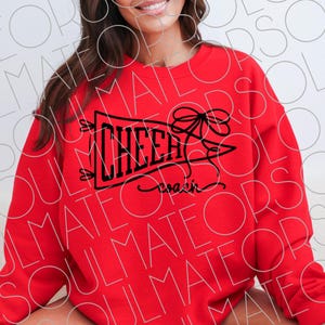 May include: A red sweatshirt with the word "CHEER" in black block letters inside a banner, with a bow and the word "coach" in script. The sweatshirt is a solid red color.