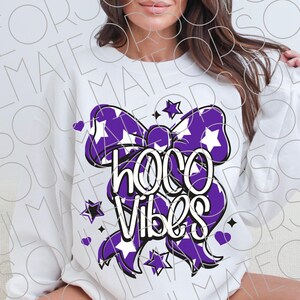 May include: White sweatshirt featuring a large purple bow with white star patterns. The words "Hoco Vibes" are written in white script within the bow design. Small purple hearts and stars surround the bow.
