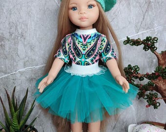 May include: A doll with long brown hair wearing a teal beret, a turquoise and black patterned shirt, a teal tulle skirt, white socks with lace trim, and blue sneakers. The doll is standing on a white crocheted doily next to a small stuffed bear.
