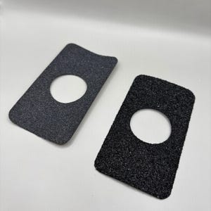 Könnte beinhalten: Zwei rechteckige, strukturierte, dunkelgraue Pads mit einem kreisförmigen Loch in der Mitte. Eines ist hellgrau, das andere schwarz. Die Pads haben abgerundete Ecken vor weißem Hintergrund.