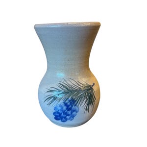 May include: A beige ceramic vase with a flared top and a rounded body. The vase is decorated with a cluster of blue grapes and green leaves. The vase is approximately 15 cm tall.