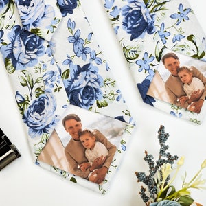 May include: Two white ties with a blue floral pattern. Each tie has a photo of a man and a child in a white frame.
