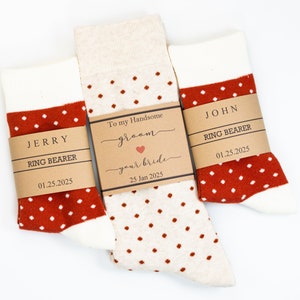 May include: Two pairs of white socks with red polka dots and brown paper tags. The tags have the text "JERRY RING BEARER 01.25.2025" and "JOHN RING BEARER 01.25.2025". The larger tag also has the text "To my Handsome groom your bride 25 Jan 2025".