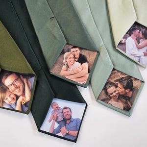 May include: Several green neckties with personalized photo inserts. The ties vary in shades of green, with images of people displayed on the front. The photos show couples and families. The ties are arranged on a white surface.