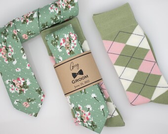 May include: A green floral patterned tie and matching pocket square with a brown gift tag that reads "Greg GROOM June 25, 2022".  A pair of green and pink argyle socks.