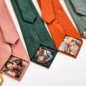 Puede incluir: Una colecci&oacute;n de corbatas de colores, cada una con un color s&oacute;lido diferente, incluyendo rosa, verde, naranja y gris. Cada corbata presenta una foto personalizada impresa en la parte posterior. Las corbatas est&aacute;n dispuestas sobre una superficie blanca.