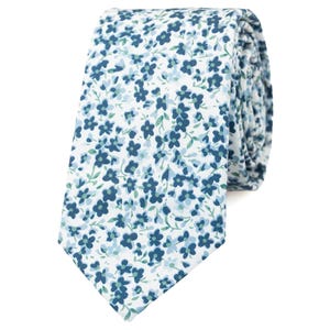 Peut inclure: Une cravate à fond blanc ornée d'un motif dense et répétitif de petites fleurs à cinq pétales dans des tons variés de bleu marine, bleu clair et vert doux. Le tissu présente une texture lisse et est plié en un rouleau bien ordonné.