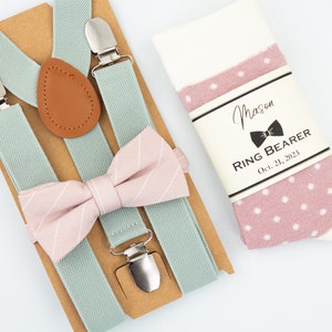 May include: A set of accessories including light blue suspenders, a pink striped bow tie, and a pair of white and pink polka dot socks. The socks have a label that reads "Mason Ring Bearer Oct. 21, 2023".