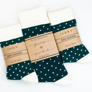May include: Three pairs of socks with a white top and toe, and a dark green polka dot pattern. Each pair has a brown paper band with text, including names like "John" and "Jerry", and the date "01.25.2025". One band reads "To my Handsome groom your bride".