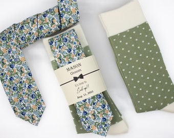 May include: A wedding gift set for the groom, featuring a floral patterned tie and a pair of green socks with white polka dots. The gift tag reads "MASON Groom It's time to Suit up!! Aug. 11, 2023".
