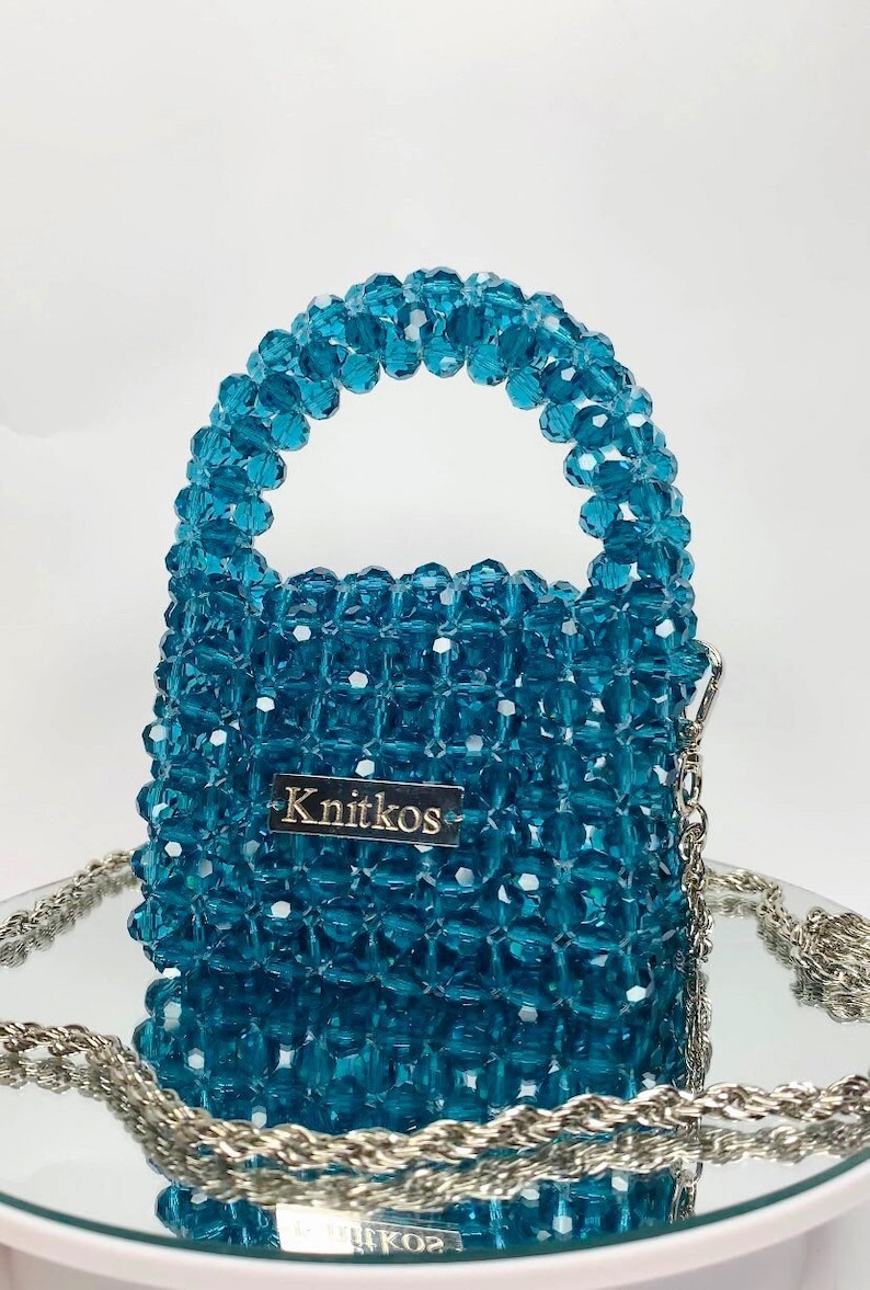 May include: A small turquoise beaded handbag with a silver chain strap and a silver tag that reads "Knitkos".