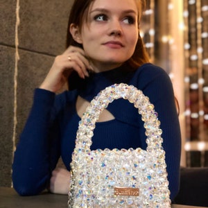 May include: A clear crystal beaded handbag with a gold chain strap and a gold logo that says "knitlos".
