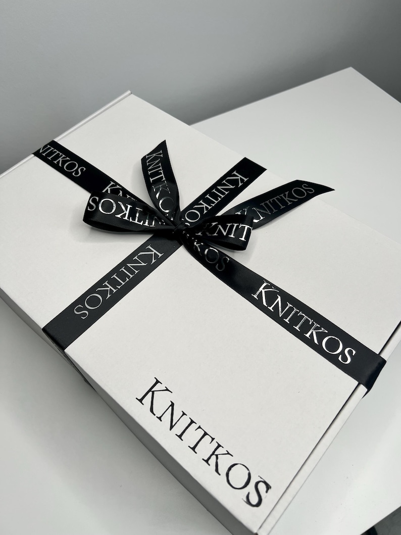 May include: A white gift box with a black ribbon tied in a bow. The ribbon has the word "KNITKOS" printed on it in a silver font.