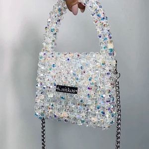 May include: A small, white beaded handbag with a silver chain strap and a black label that reads "k.nitkos".