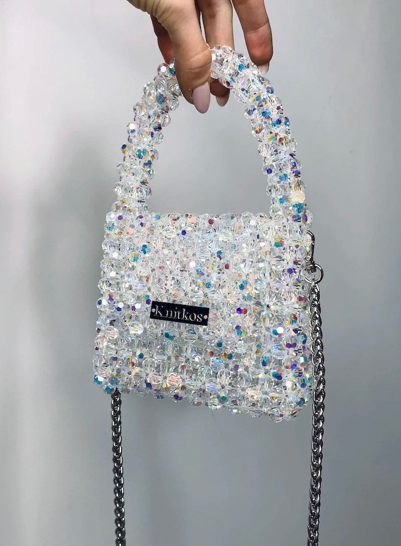 May include: A small, white beaded handbag with a silver chain strap and a black label that reads "k.nitkos".
