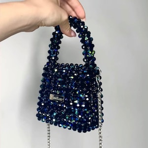 May include: A small, dark blue beaded handbag with a silver chain strap. The bag has a label that reads "Kuilos".