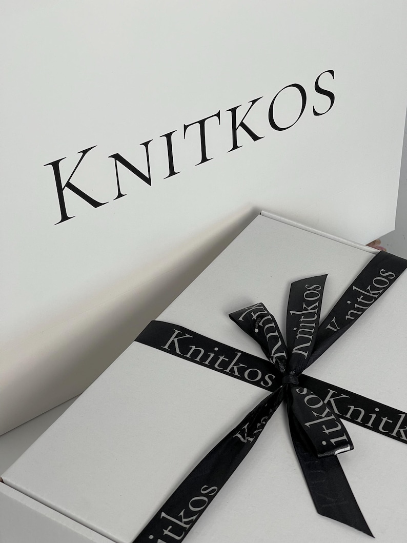 May include: A white gift box with a black ribbon tied in a bow. The ribbon has the word "Knitkos" printed on it in a gray font.