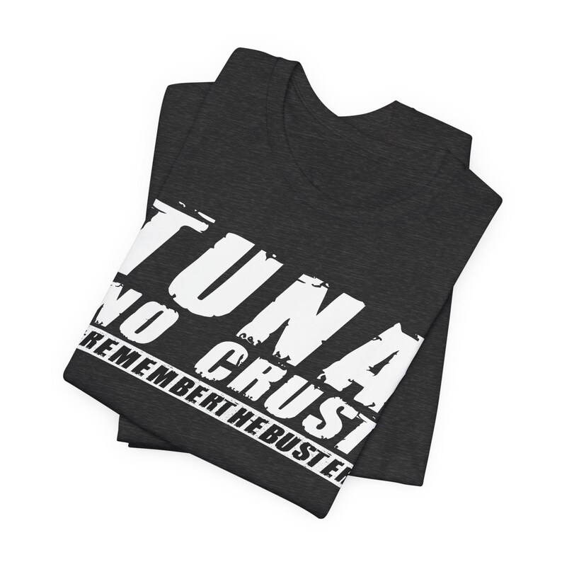 Pu&ograve; includere: Una t-shirt grigio antracite scuro con scritte bianche dall'effetto usurato che recitano TUNA NO CRUST REMEMBER THE BUSTER. La maglietta &egrave; piegata e presenta un girocollo e maniche corte, realizzate in un tessuto dall'aspetto testurizzato.
