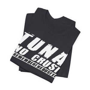 Pu&ograve; includere: Una t-shirt nera a maniche corte con testo bianco in stile consumato stampato sul davanti. Il testo recita TUNA NO CRUST REMEMBER THE BUSTER in un carattere grassetto e maiuscolo. Il capo &egrave; piegato ordinatamente per mostrare chiaramente il design.