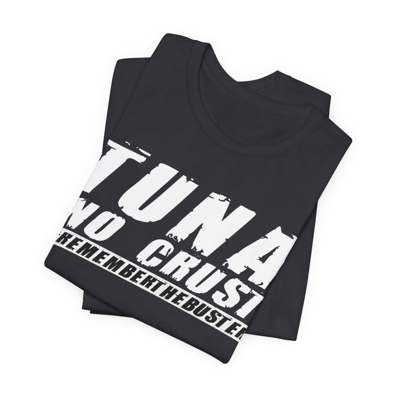 Pu&ograve; includere: Una t-shirt nera a maniche corte con testo bianco in stile consumato stampato sul davanti. Il testo recita TUNA NO CRUST REMEMBER THE BUSTER in un carattere grassetto e maiuscolo. Il capo &egrave; piegato ordinatamente per mostrare chiaramente il design.