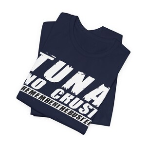 Pu&ograve; includere: Una t-shirt blu navy piegata con testo bianco in stile consumato stampato sul davanti. Il testo recita TUNA NO CRUST e REMEMBER THE BUSTER in un carattere grassetto senza grazie. Il capo &egrave; piegato ordinatamente, mostrando chiaramente il design.