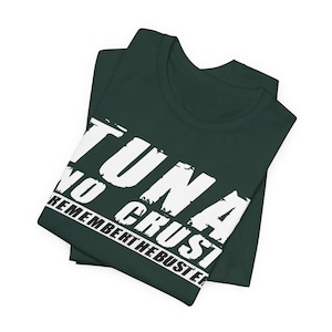 Pu&ograve; includere: Una t-shirt verde scuro con testo bianco dall'aspetto consumato che recita TUNA NO CRUST REMEMBER THE BUSTER. La maglietta &egrave; piegata ordinatamente, mettendo in risalto la stampa grafica sulla parte anteriore del petto del capo.